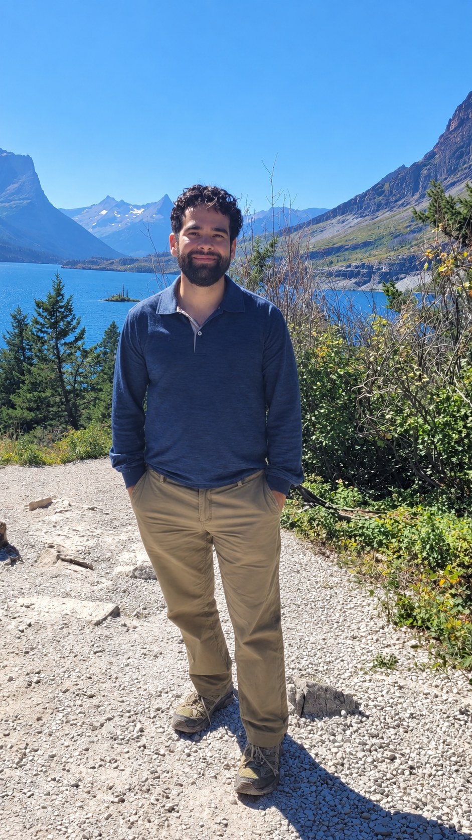 Dane Christensen standing by a mountain lake in a blue shirt and khaki pants